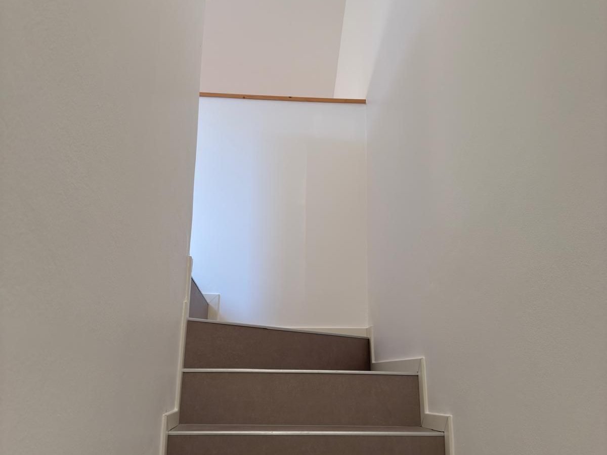 Vano scala interno tinteggiato di bianco, con gradini color tortora e corrimano in legno chiaro