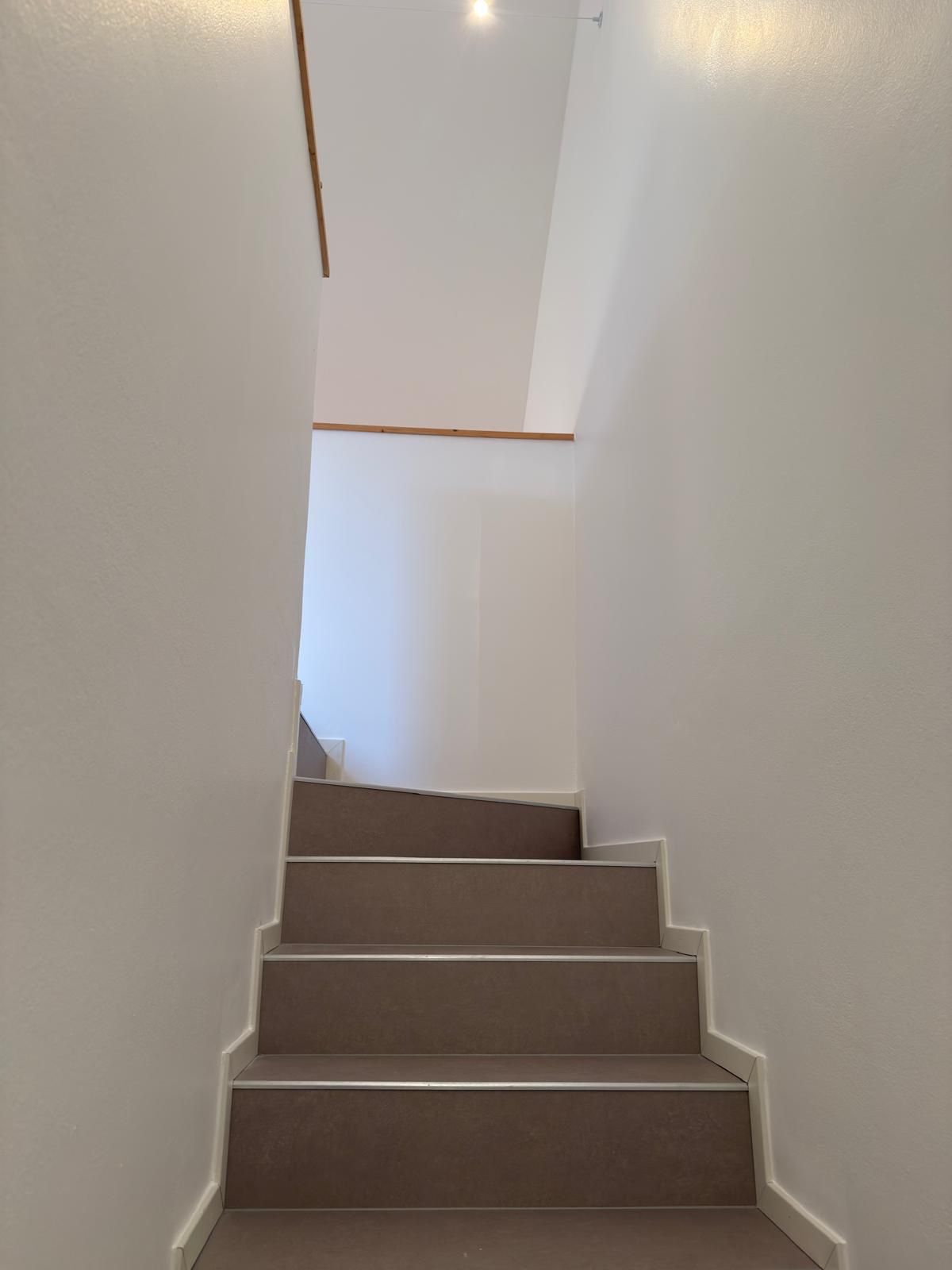 Vano scala interno tinteggiato di bianco, con gradini color tortora e corrimano in legno chiaro