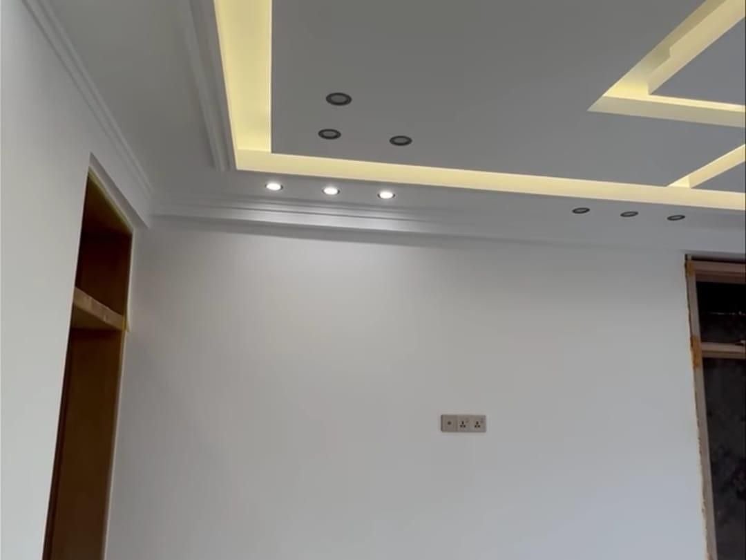 Soffitto in cartongesso con velette geometriche, luce LED calda a scomparsa e faretti a incasso, sopra una parete bianca appena tinteggiata