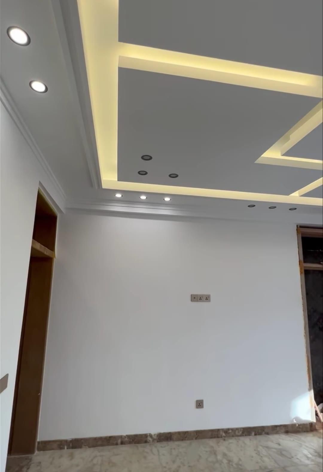 Soffitto in cartongesso con velette geometriche, luce LED calda a scomparsa e faretti a incasso, sopra una parete bianca appena tinteggiata