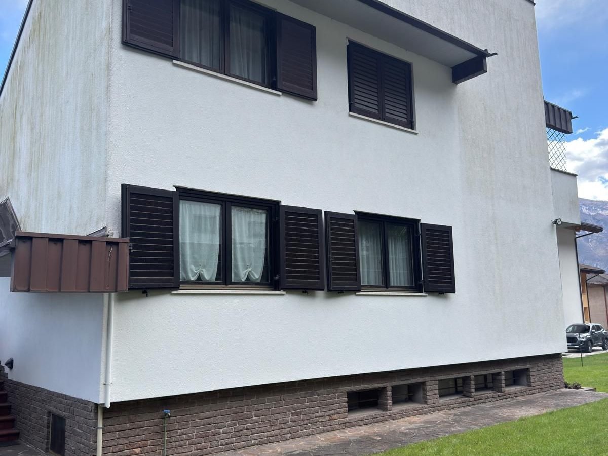 Villa a due piani con facciata chiara, scuri in legno scuro e zoccolatura in mattoni, ripresa dal prato del giardino