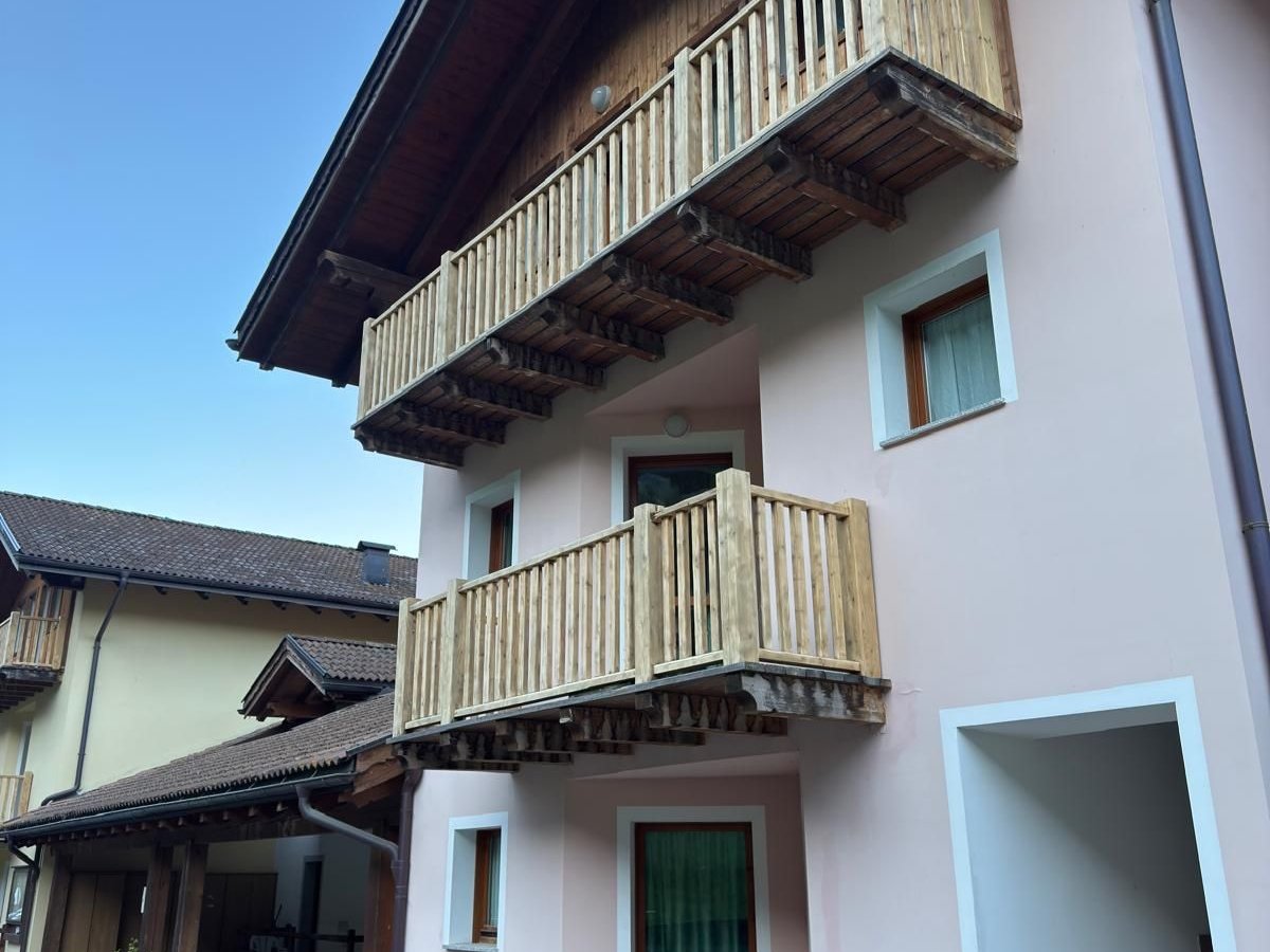 Casa di montagna con facciata rosa antico appena tinteggiata, due balconi in legno chiaro, sporto del tetto in legno e scala d'ingresso