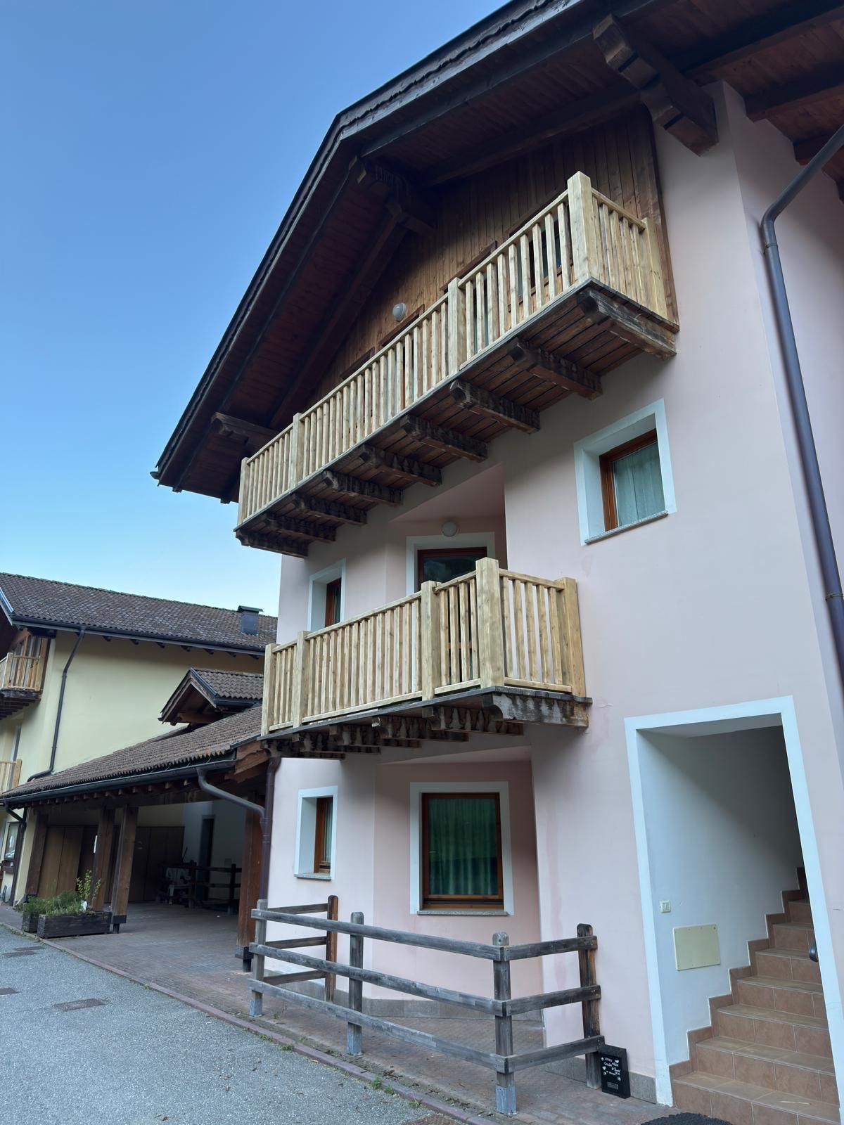 Casa di montagna con facciata rosa antico appena tinteggiata, due balconi in legno chiaro, sporto del tetto in legno e scala d'ingresso