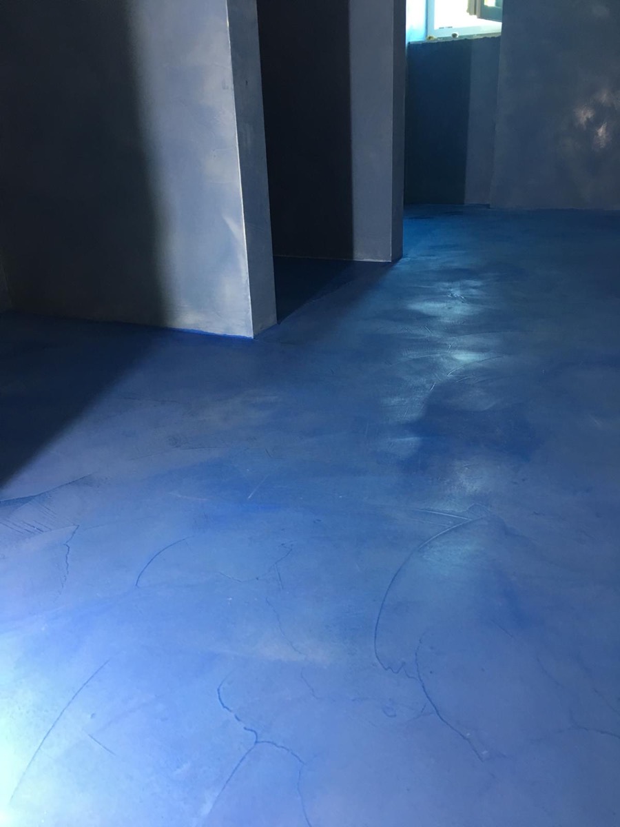 Ambiente vuoto con pavimento in resina continua blu e pareti grigio-blu attraversati da luce radente