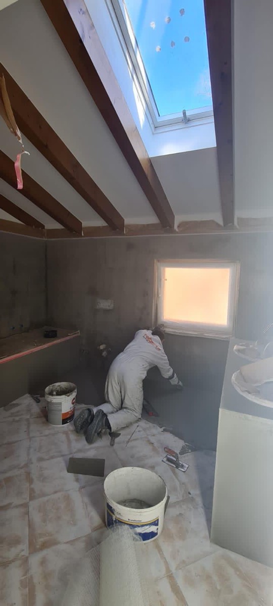 Operatore stende la rasatura grigia su una parete di un bagno in mansarda