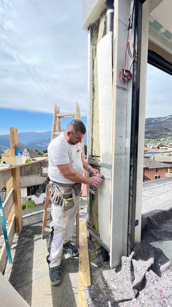 Posa di pannelli isolanti su profili metallici in quota, con le montagne sullo sfondo