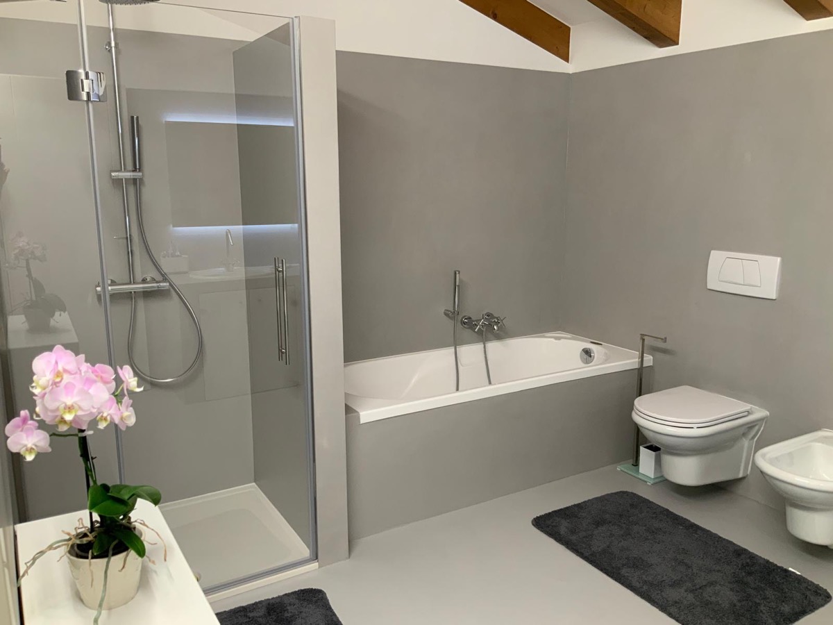 Bagno finito con superfici continue grigie, vasca da bagno, box doccia in vetro e orchidea rosa in primo piano