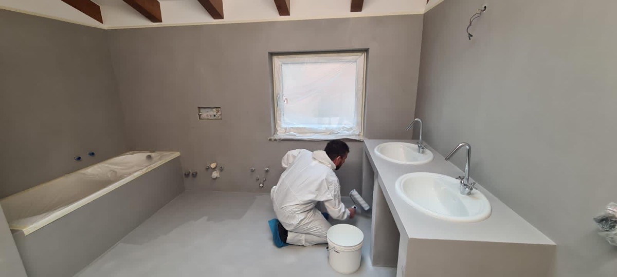 Bagno rifinito in resina grigia con pittore che stende a rullo vicino alla finestra