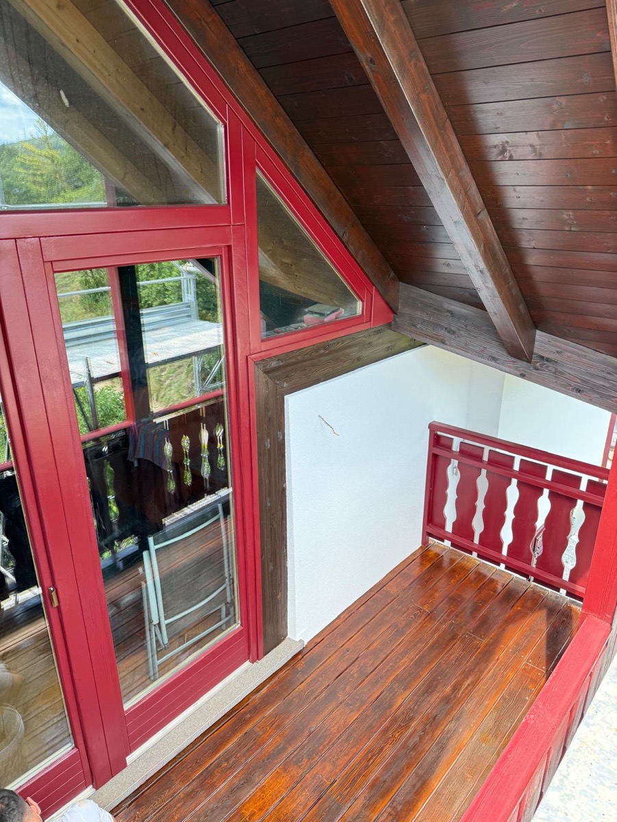 Balcone esterno con serramenti e ringhiera in legno rosso, tavolato verniciato e parete bianca