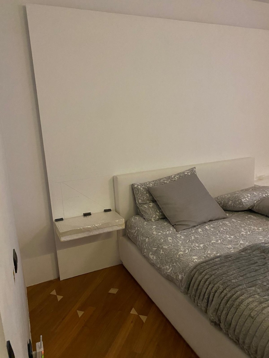 Camera da letto con parete bianca appena tinteggiata e mensola comodino sospesa