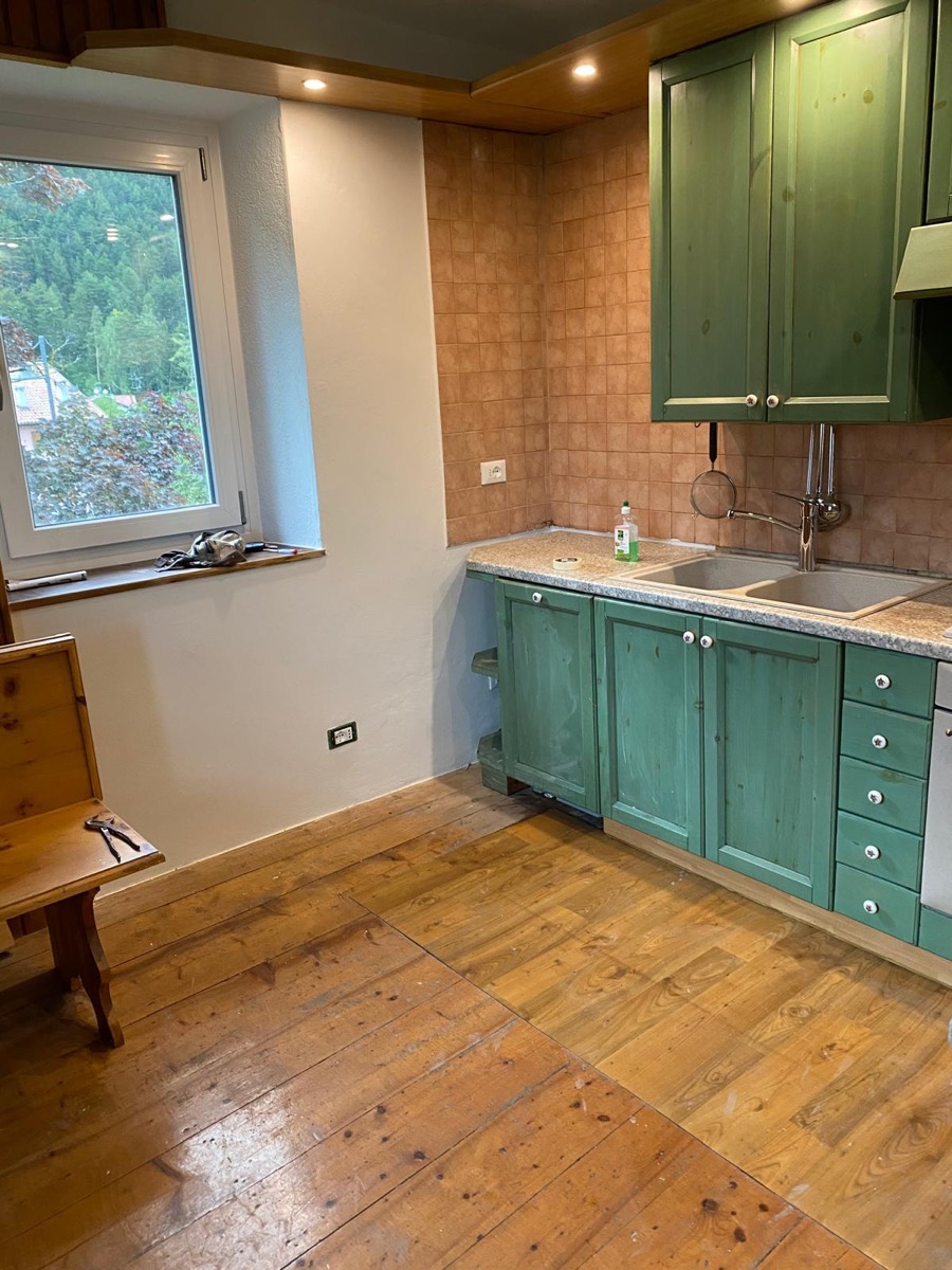 Cucina con pareti bianche appena tinteggiate, mobili in legno verde e pavimento in tavole di legno