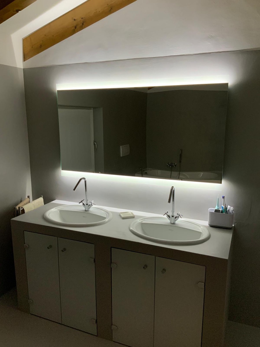 Mobile con doppio lavabo e specchio retroilluminato acceso in un bagno grigio, foto serale