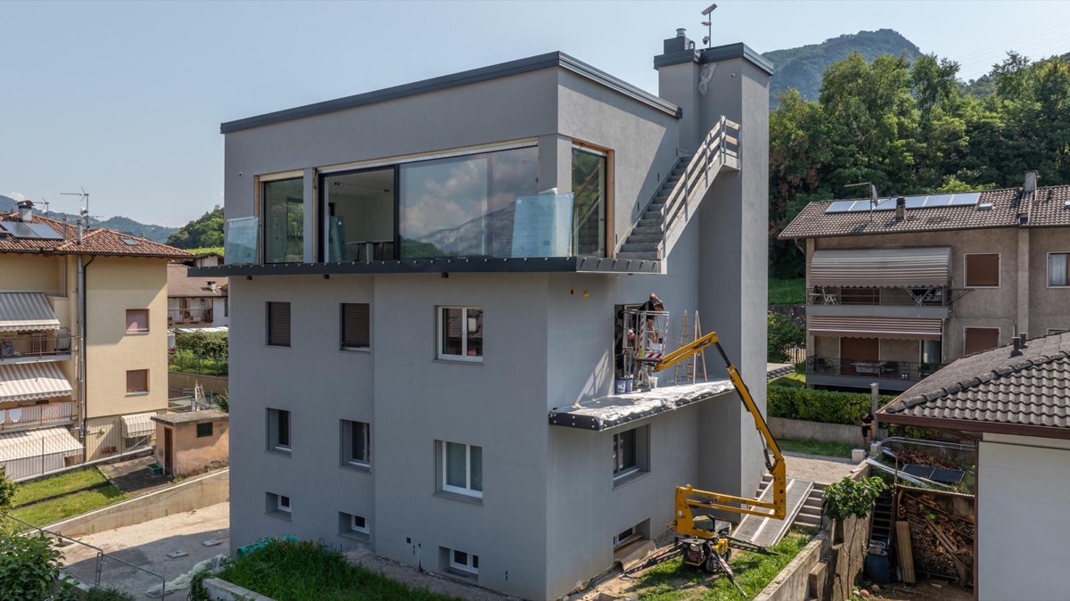 Facciata grigia di un edificio moderno con piattaforma aerea e operai al lavoro sul balcone