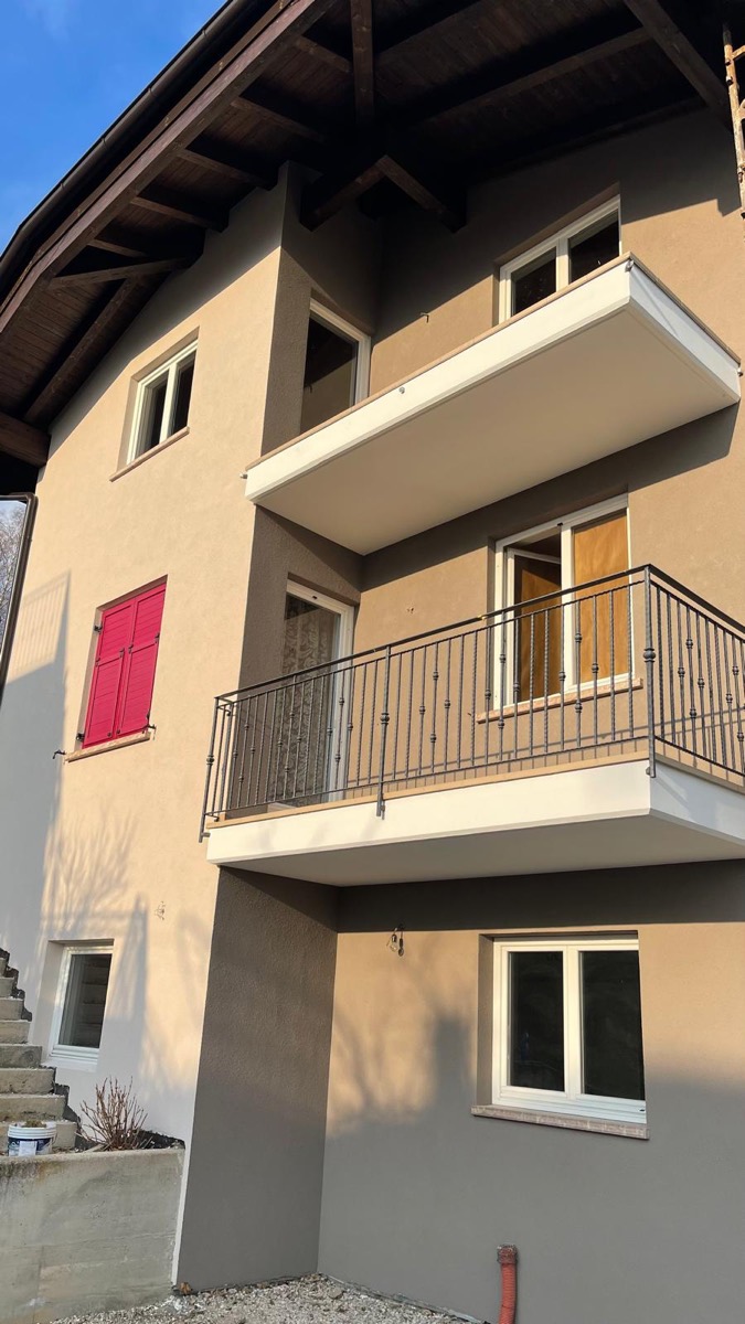 Facciata esterna tinteggiata beige con riquadri grigio tortora, persiana rossa e balconi con ringhiera