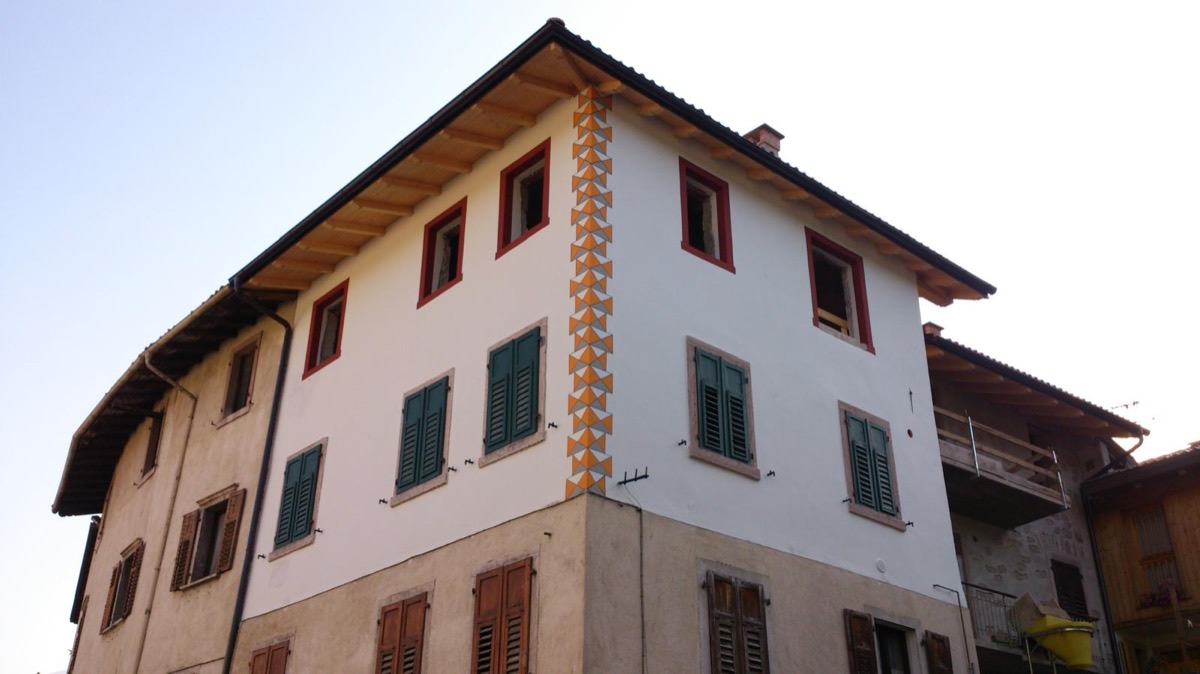 Facciata di edificio tinteggiata di bianco con decoro a triangoli arancio sullo spigolo e scuri verdi