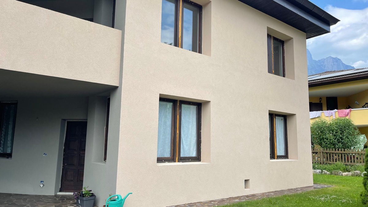 Facciata di casa tinteggiata color sabbia con sottoportico grigio e finestre con telai in legno scuro