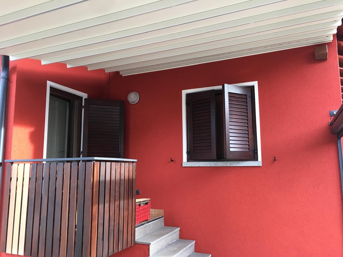 Parete esterna di casa tinteggiata in rosso con scuri in legno scuro, sottotetto bianco e scala in pietra