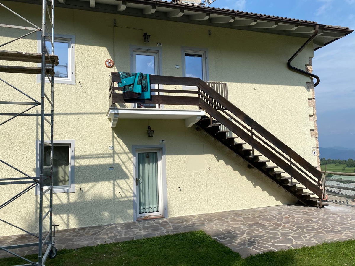 Facciata tinteggiata giallo chiaro con scala esterna in legno, trabattello metallico e cielo sereno