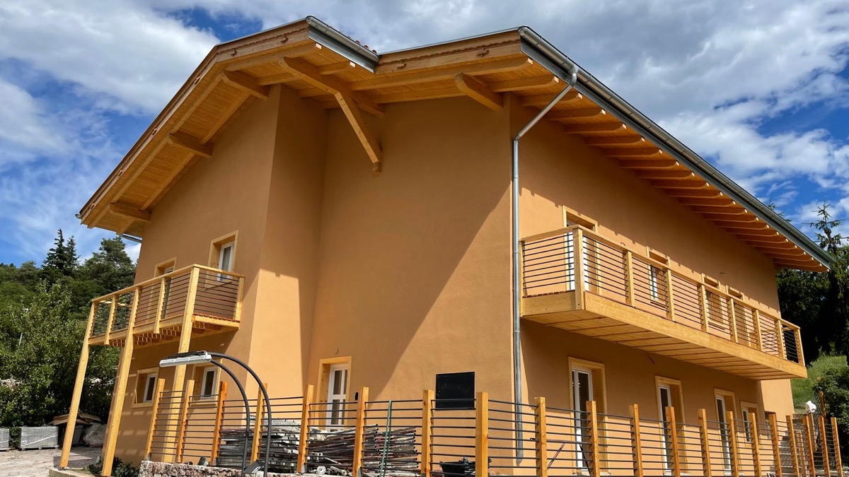 Edificio con facciata tinteggiata color ocra, grande tetto in legno a vista e balconi in legno
