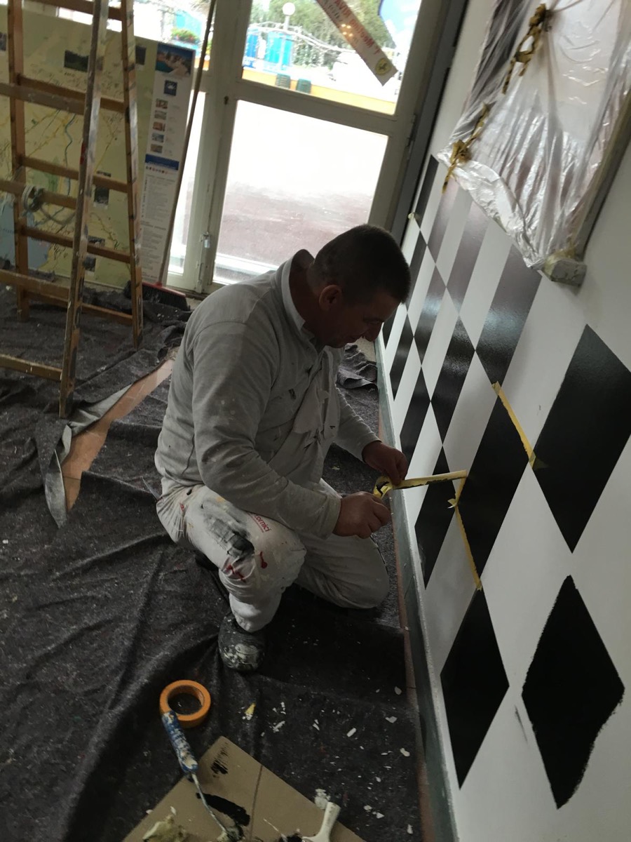 Imbianchino al lavoro che rifinisce una parete decorata a rombi bianchi e neri
