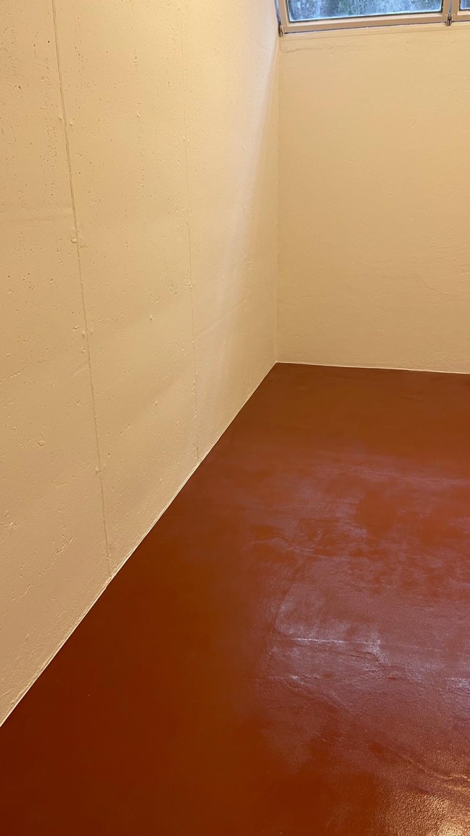 Locale interrato vuoto con pavimento resinato rosso mattone lucido e pareti color crema