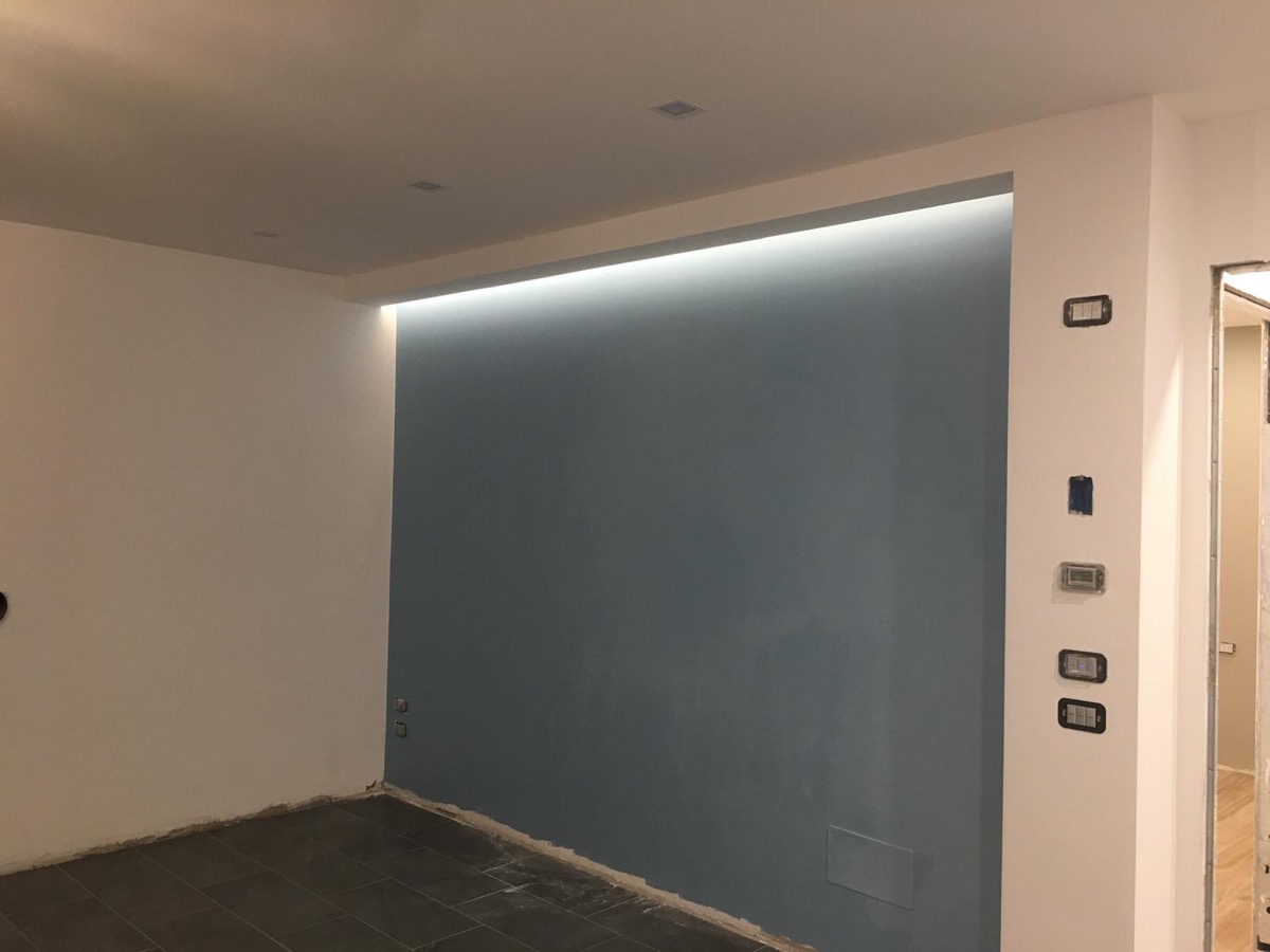 Parete azzurro-grigia dentro nicchia in cartongesso con striscia LED a scomparsa e pavimento scuro