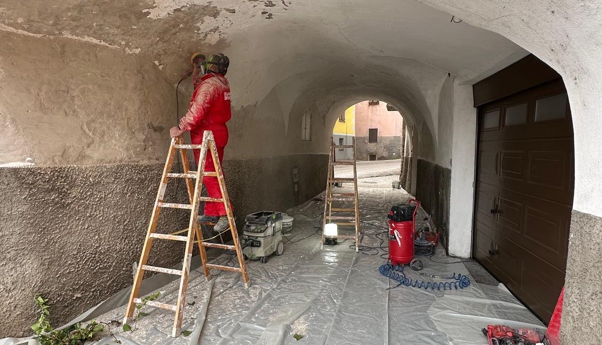 Operaio su scala rifa l'intonaco della volta di un androne passante di un edificio storico