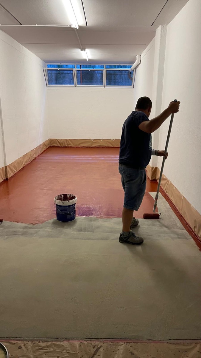 Operaio visto di spalle stende con rullo a manico lungo la resina rossa sul pavimento