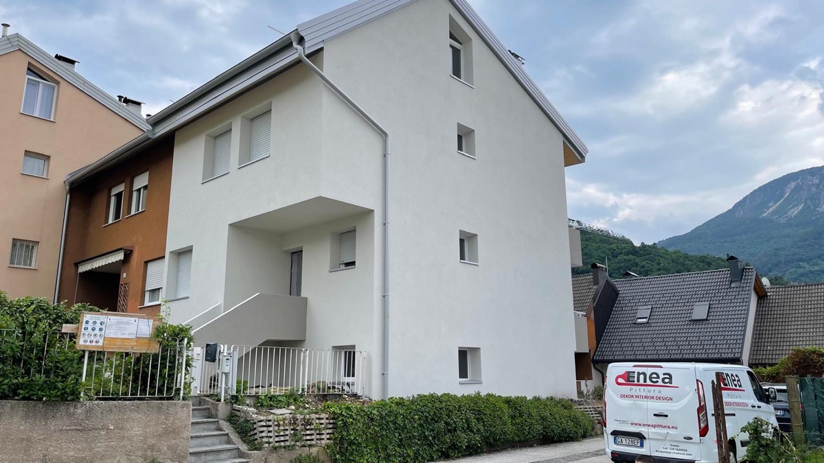 Palazzina bianca appena tinteggiata con furgone Enea Pittura davanti e montagna sullo sfondo