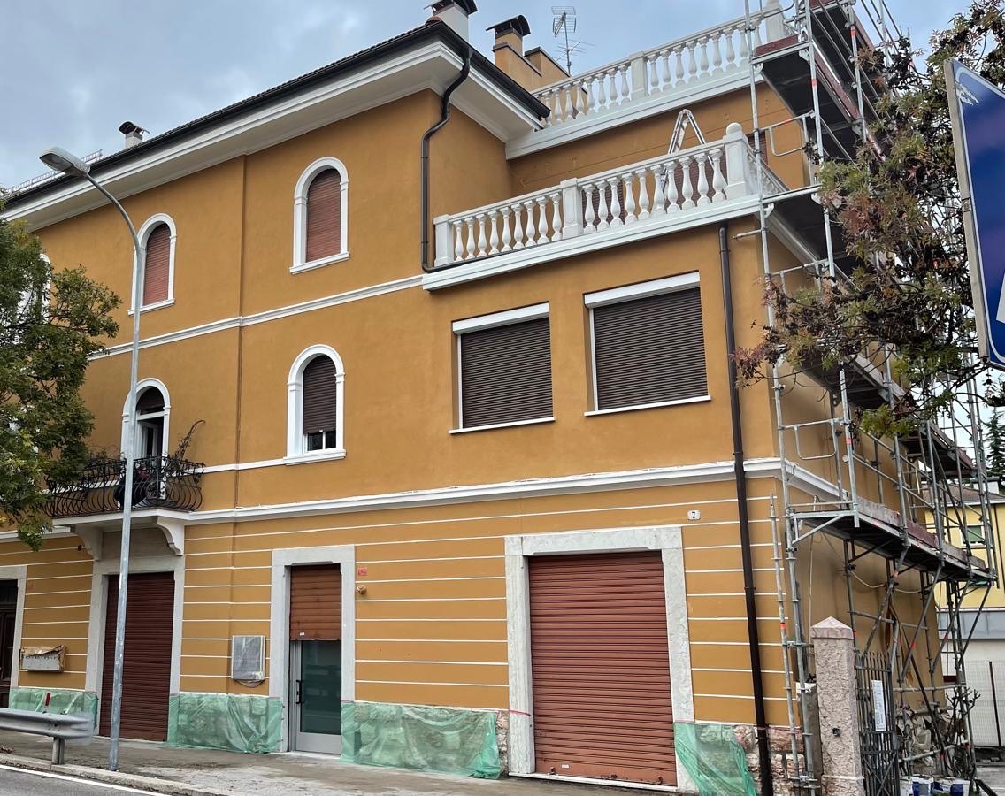 Facciata di palazzina tinteggiata giallo ocra con cornici e fasce bianche e ponteggio laterale