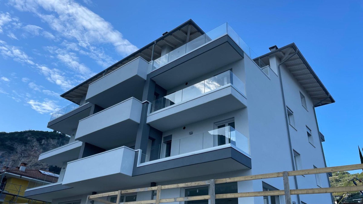 Palazzina moderna con facciata bianca e grigia e parapetti in vetro, ripresa dal basso col cielo blu