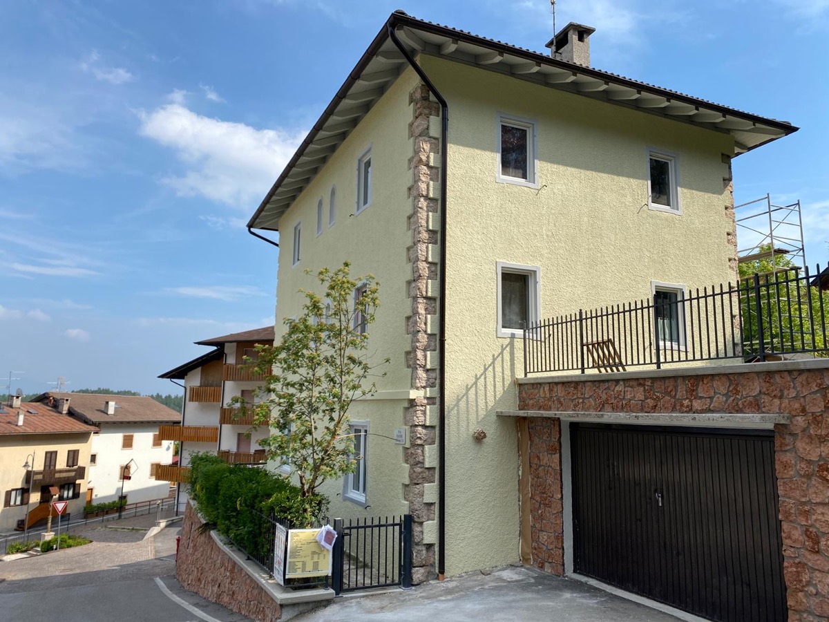 Facciata di una palazzina a tre piani tinteggiata di verde chiaro, con cantonali in pietra, gronda in legno e garage al piano strada