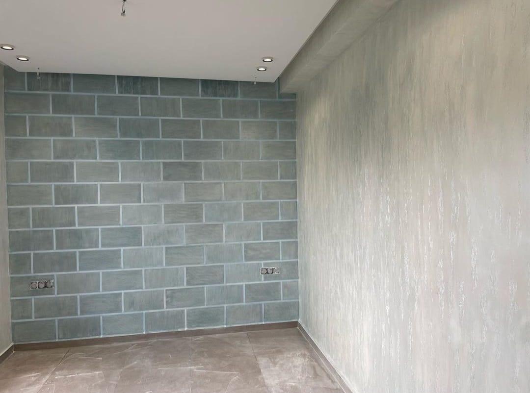 Stanza finita con parete decorata a finti conci verde-grigio e parete attigua effetto spatolato chiaro