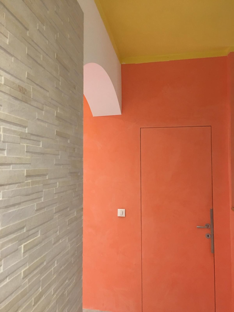 Angolo con parete effetto spatolato corallo, porta filomuro, soffitto giallo e rivestimento in pietra chiara