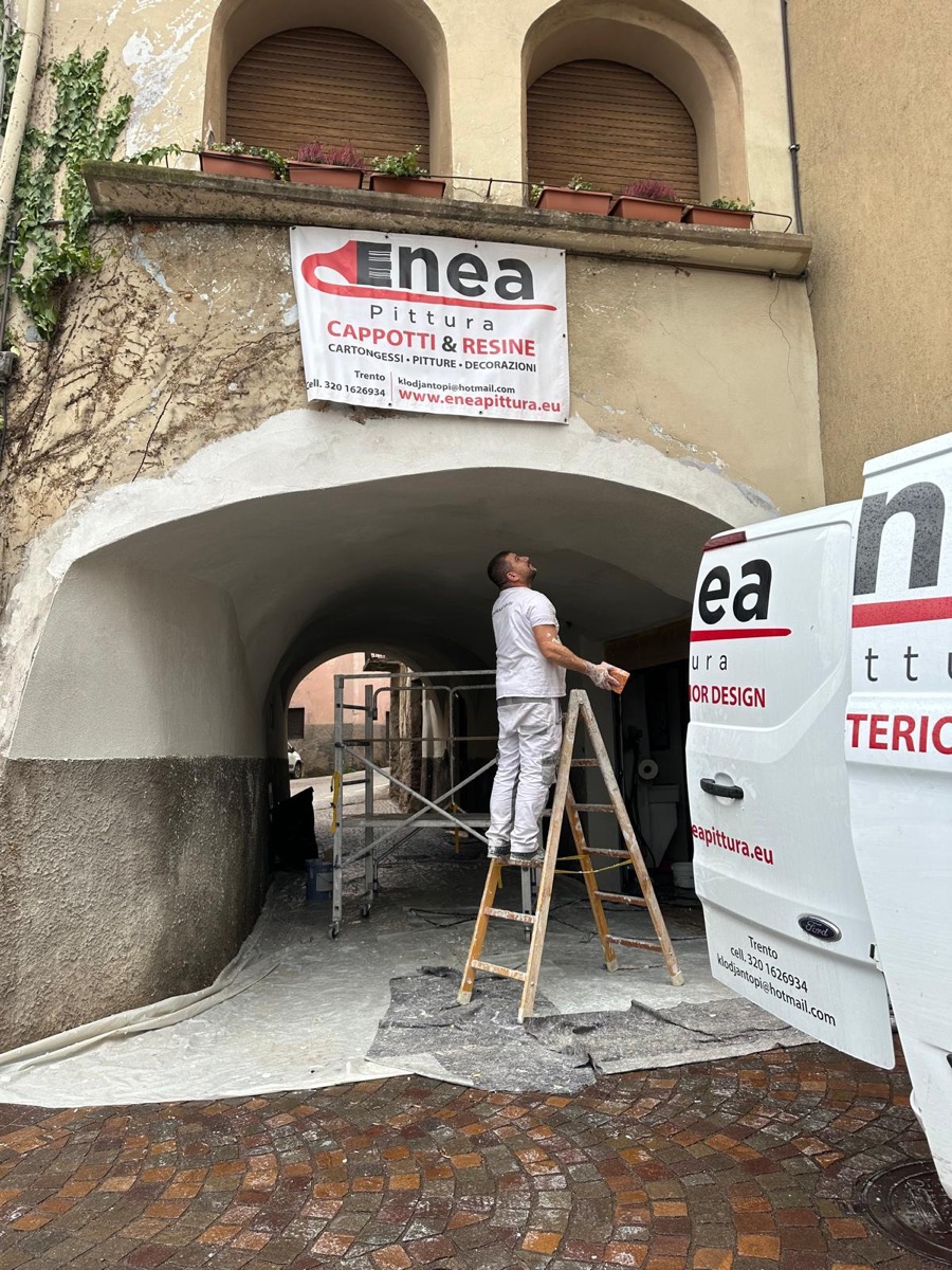 Pittore su scala rasa l'arco di un portico storico accanto al furgone Enea Pittura