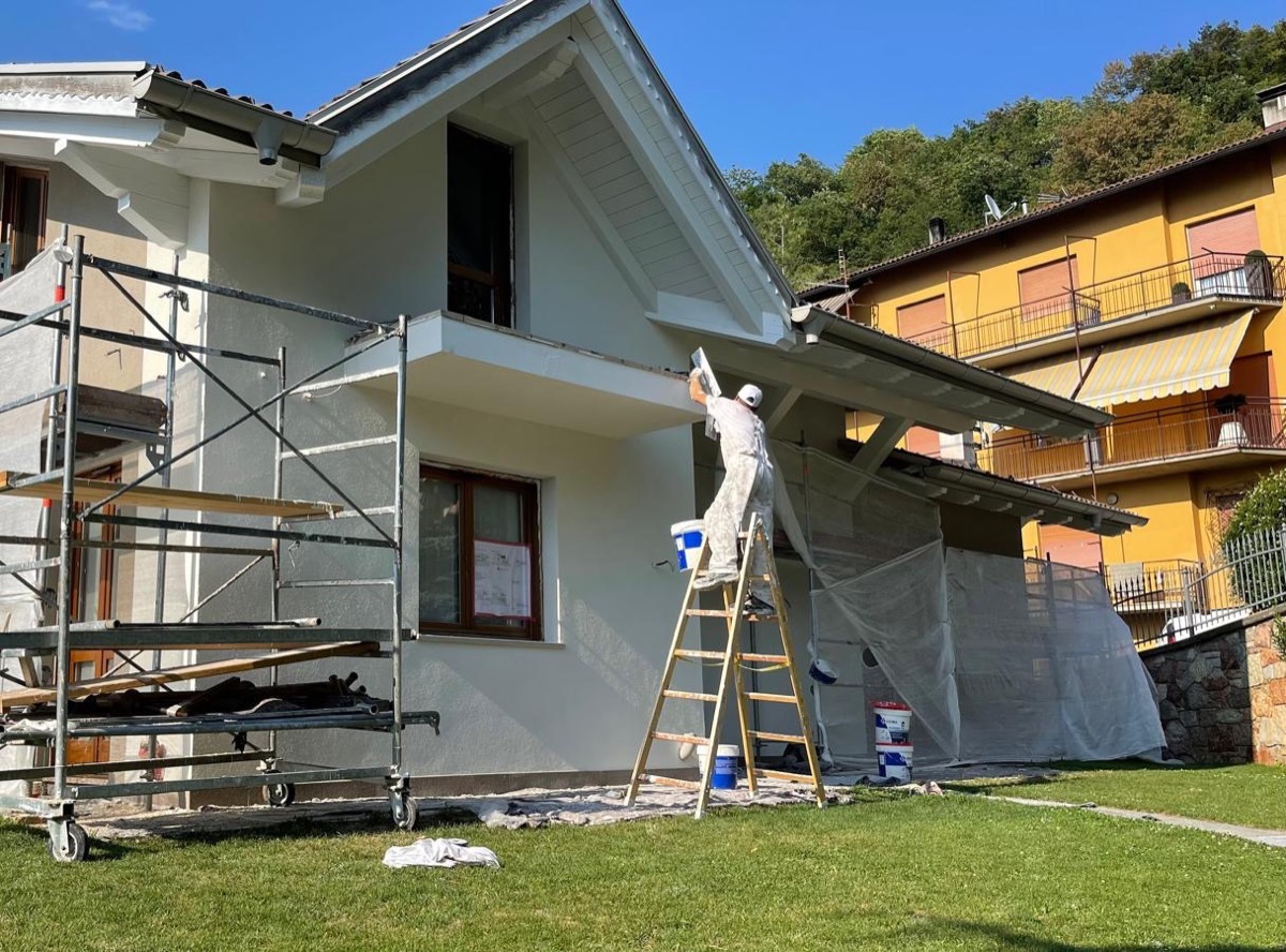 Pittore su scala rifinisce il sottotetto di una villetta con ponteggio e teli di protezione