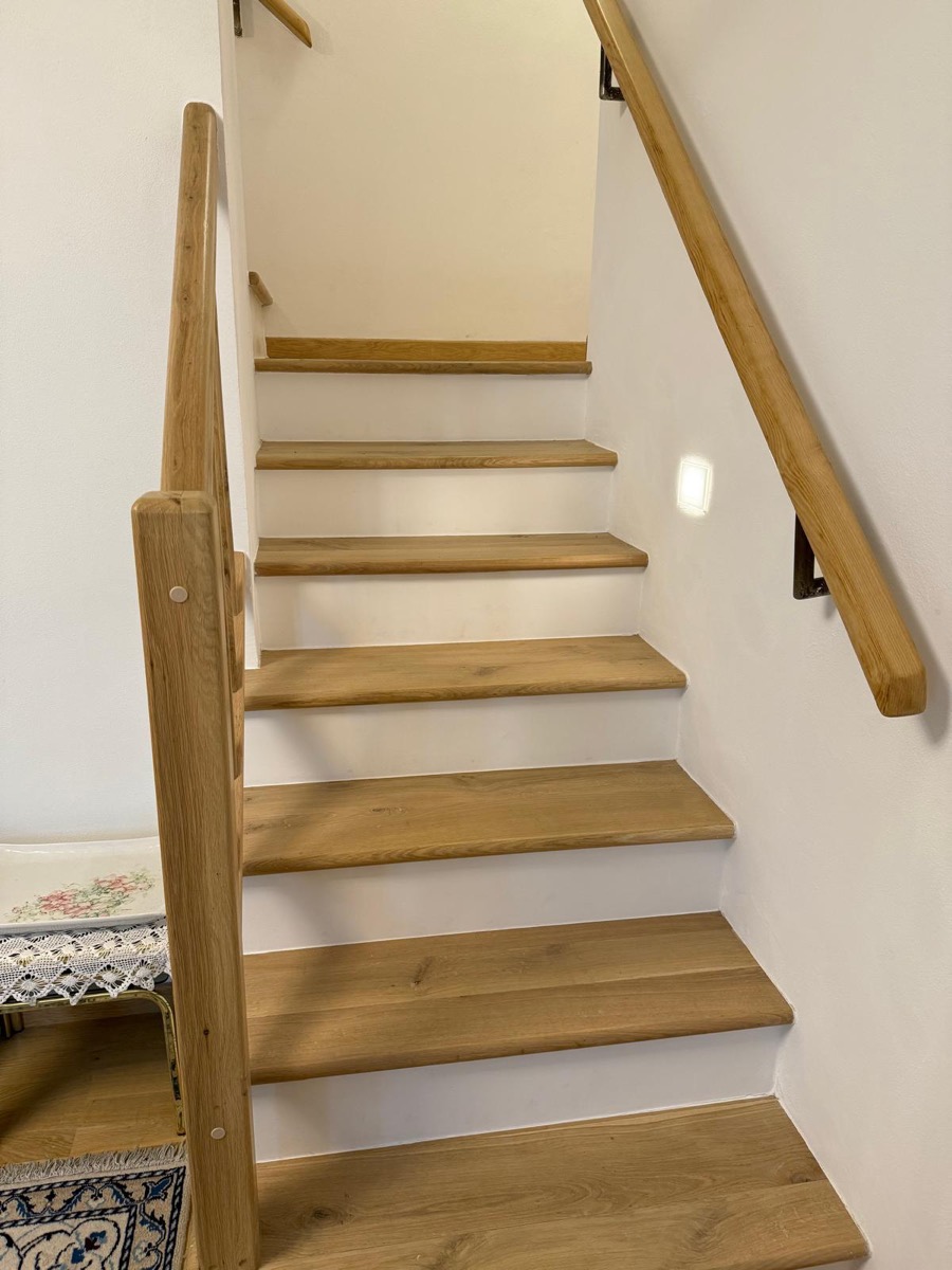 Scala interna con gradini in legno chiaro, corrimano in legno e pareti bianche tinteggiate