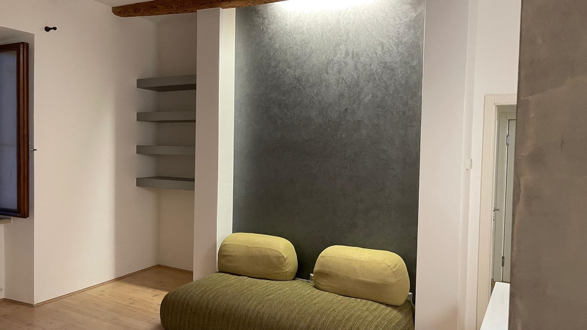 Soggiorno con parete decorativa effetto spatolato grigio antracite, mensole a incasso e divano verde