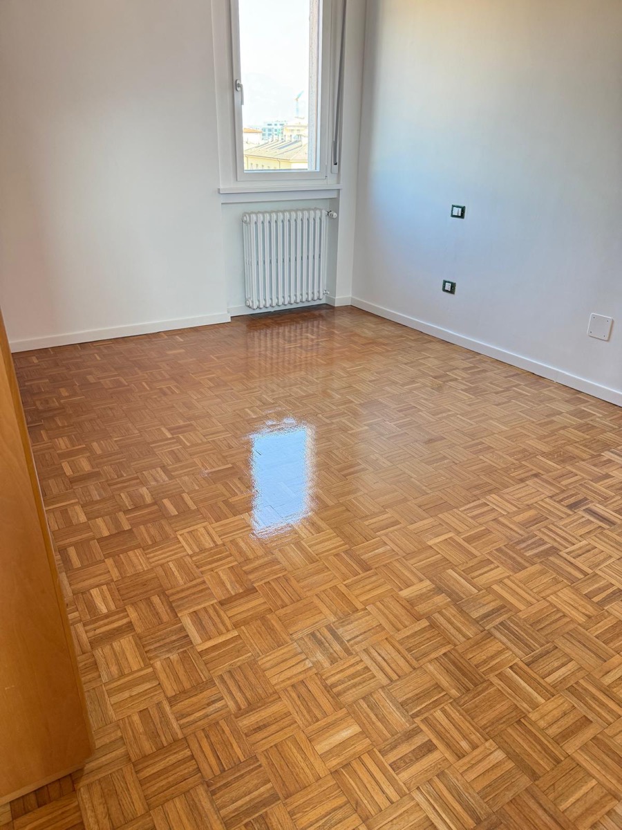 Stanza vuota con pareti tinteggiate di bianco, parquet a quadrotte lucido e radiatore