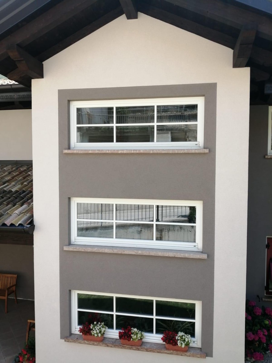 Facciata beige con riquadro tortora attorno a tre finestre in fila, davanzali in pietra e fioriere