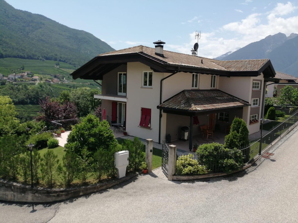 Villa con facciata tinteggiata beige e grigio, persiane rosse, colline e montagne sullo sfondo