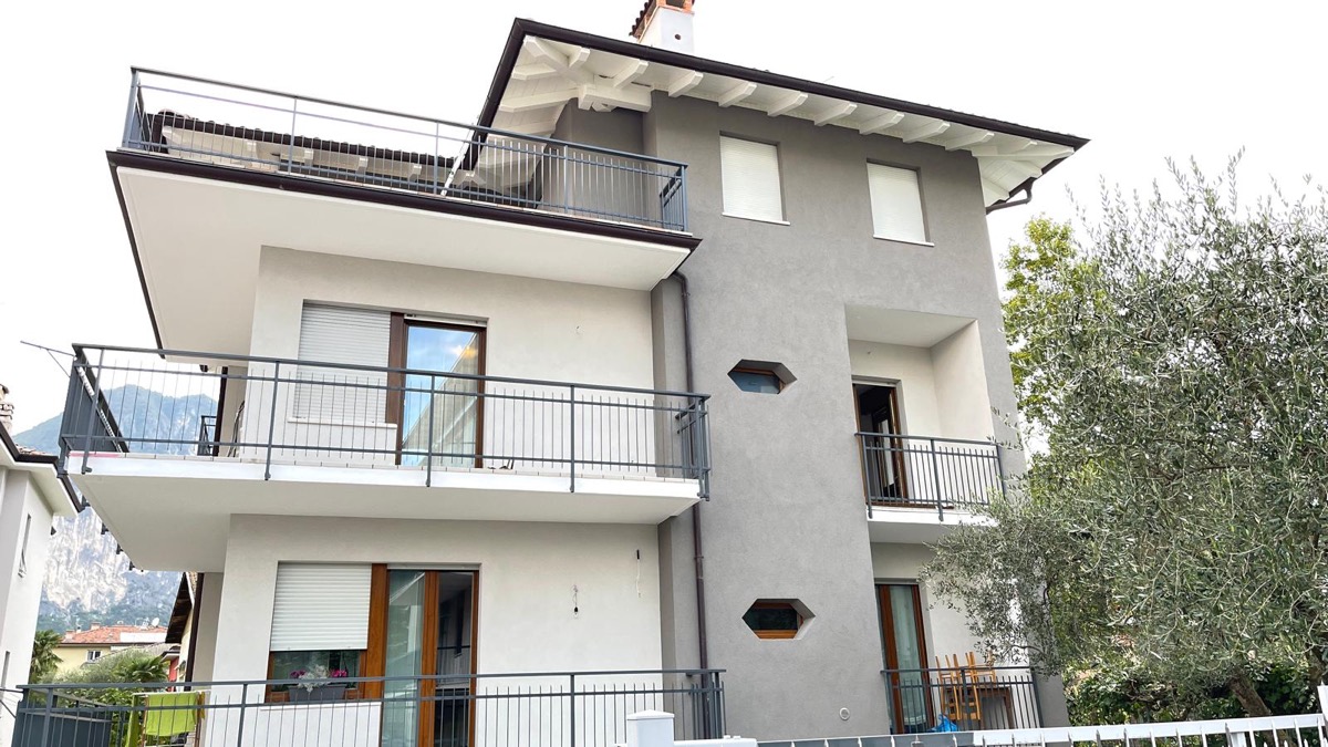 Villa con facciata tinteggiata in bianco e grigio antracite, balconi con ringhiere e un ulivo a destra