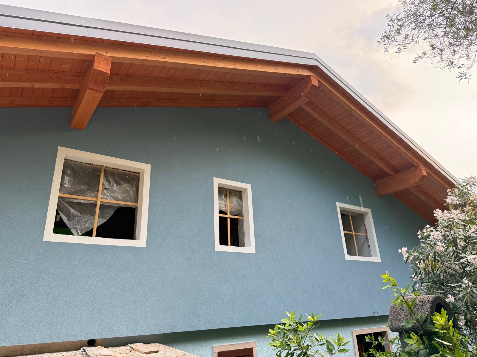 Facciata di casa con intonaco azzurro-grigio, cornici bianche alle finestre e sporto del tetto in legno