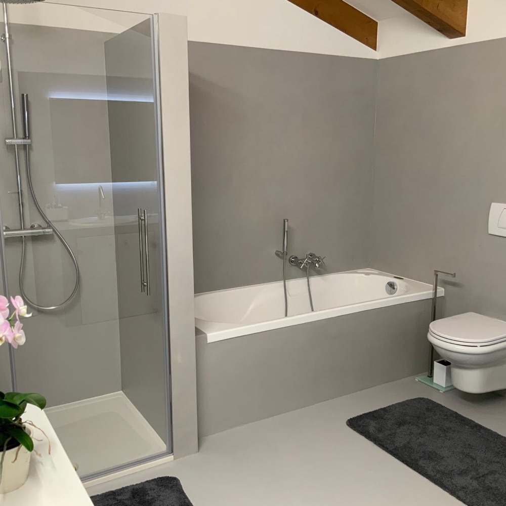 Bagno finito con superfici continue grigie, vasca da bagno, box doccia in vetro e orchidea rosa in primo piano