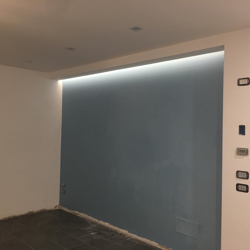 Parete azzurro-grigia dentro nicchia in cartongesso con striscia LED a scomparsa e pavimento scuro