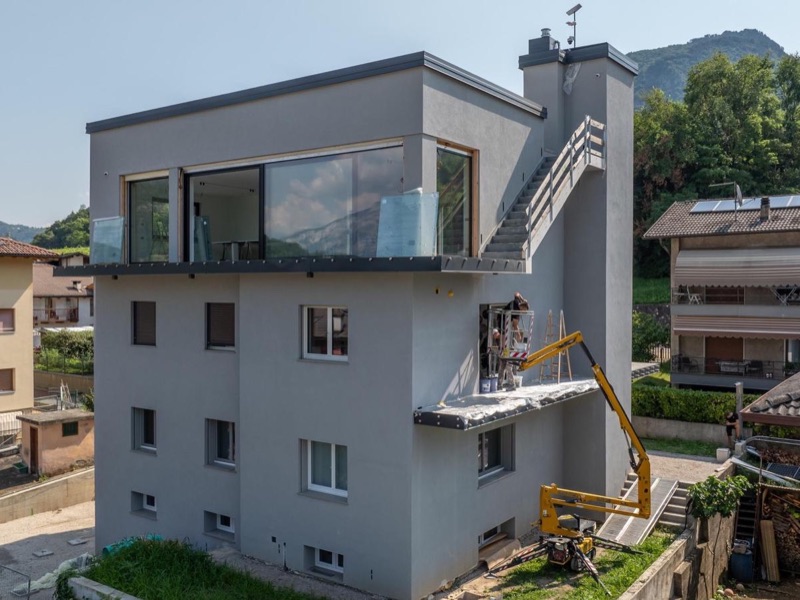 Facciata grigia di un edificio moderno con piattaforma aerea e operai al lavoro sul balcone