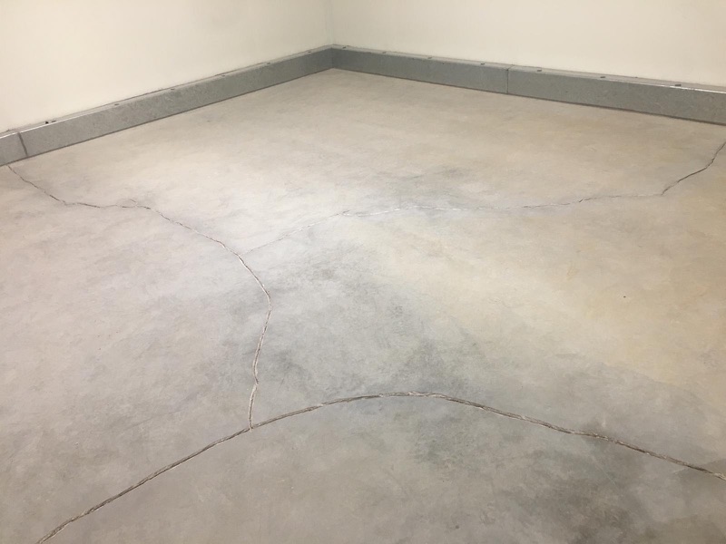 Dettaglio di pavimento continuo grigio chiaro con giunti curvi e battiscopa in metallo