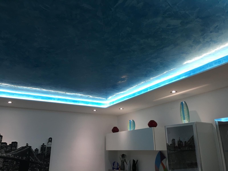 Soggiorno con soffitto decorato blu effetto spatolato, cornice luminosa a LED azzurra e faretti a incasso