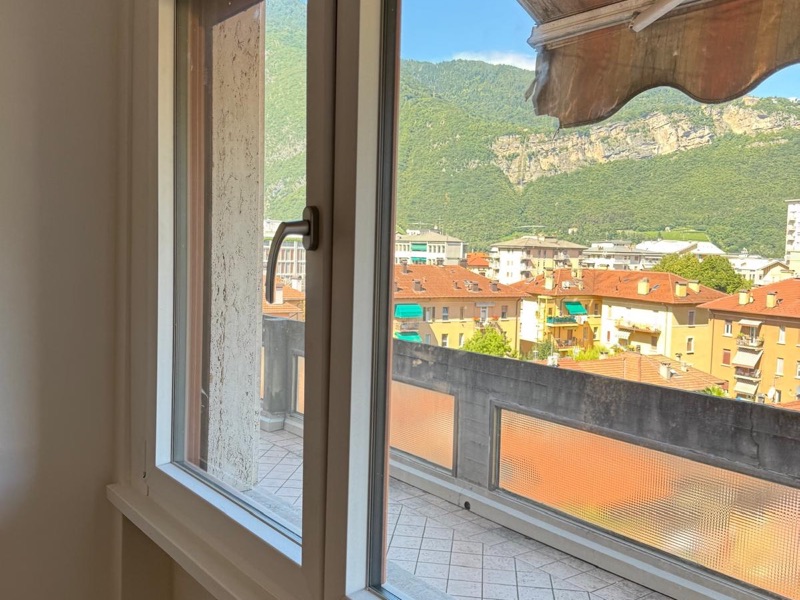 Interno tinteggiato di bianco con finestra, radiatore e vista sui tetti del paese e sulla montagna